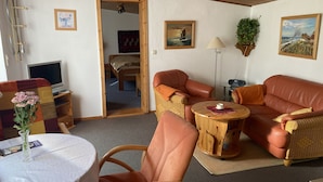 A cozy living room with a sofa, chairs, a small table, and a TV. - Vacation apartment with green garden view (Ahrenshoop)