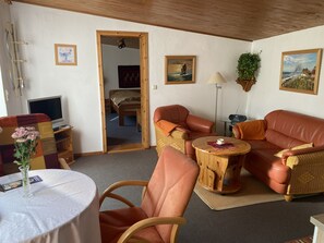 Ein gemütliches Wohnzimmer mit einer Couch, Sesseln, einem kleinen Tisch und einem Fernseher.