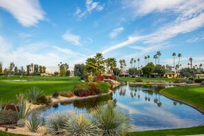 A golf course with a pond, palm trees, and a clear sky. - Large, airy mid-century condo at 7 Lakes golf club (Palm Springs)