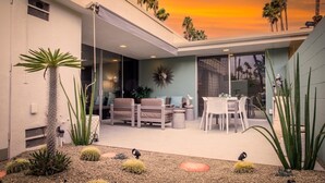 Uma casa moderna com um pátio, móveis de exterior e cactos.