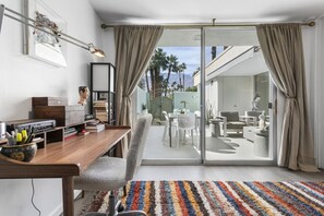 A modern room with a desk, chair, and a view of an outdoor patio with chairs and a table. - Large, airy mid-century condo at 7 Lakes golf club (Palm Springs)