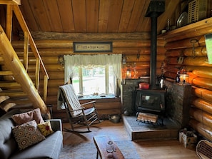 A log cabin interior with a fireplace, rocking chair, and a sign reading 'Faith Hope Love'.
