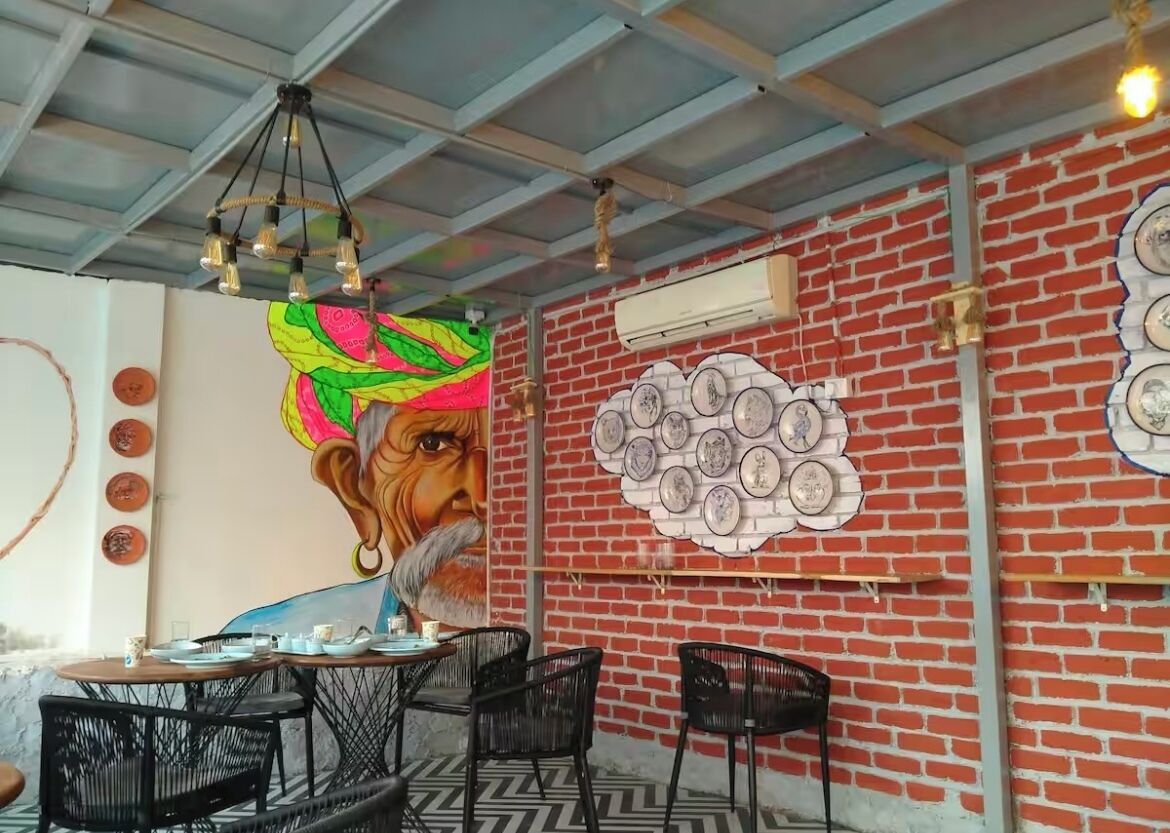 Uma área de refeições com parede de tijolos, um mural e teto com vigas aparentes.