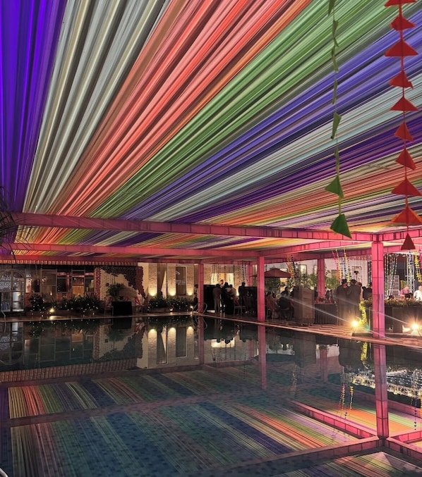 Ein großzügiger Innenbereich mit einem spiegelnden Pool, einer Decke mit farbigen Lichtleisten und einer Bar, an der sich Personen aufhalten.