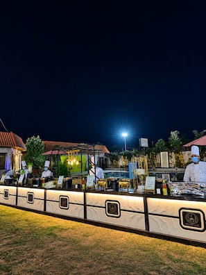 An outdoor dining area with chefs, a counter, and a pool in the background. - The Sparkle  (Jaipur)