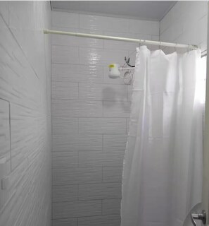 A shower with a white curtain, a white towel dispenser, and a white tiled wall.