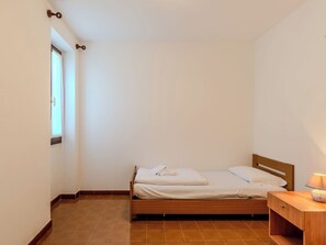 A single bed with a wooden headboard, a bedside table with a lamp, and a window with curtains. - Casa Twins by Interhome (Gravedona)