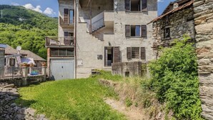 Un edificio in pietra di due piani con un balcone, un piccolo giardino e un muro in pietra.