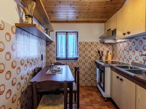A compact kitchen with a dining table, chairs, a window, and a sink. - Casa Twins by Interhome (Gravedona)