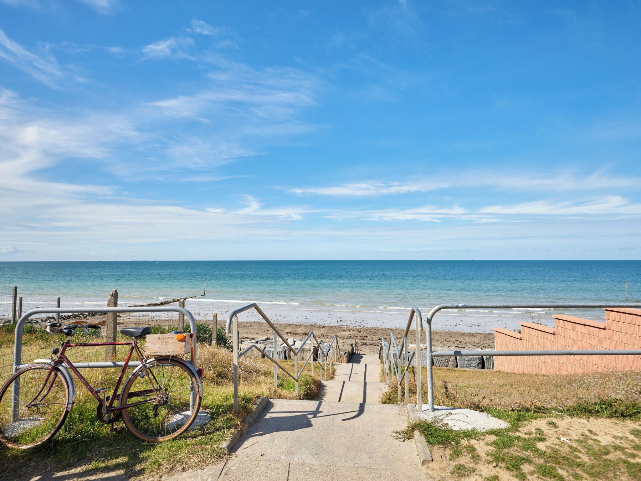 Un sentier menant à une plage, avec un vélo garé sur le côté gauche.