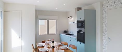 A dining area with a table set for four, a kitchen with blue cabinets, and a ceiling light fixture.