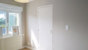 A bedroom with a white bed, a radiator, a door, and a window with a picture frame. - Dolce Vita by Interhome (Agon-Coutainville)
