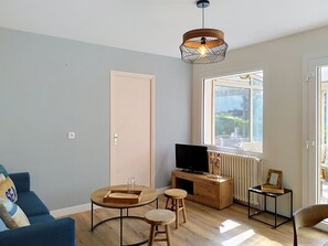 A living room with a sofa, a TV on a wooden stand, a dining table with stools, and a large window with a view. - Dolce Vita by Interhome (Agon-Coutainville)