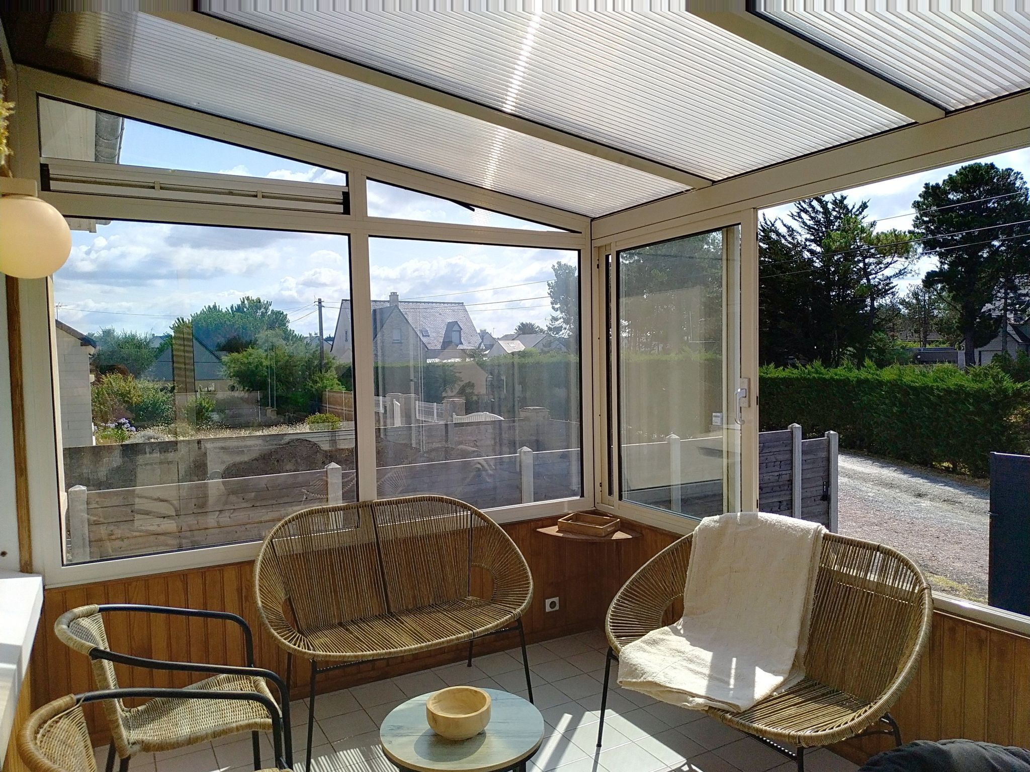 Una veranda con ampie finestre, sedie in vimini, un tavolino e vista su una zona residenziale.