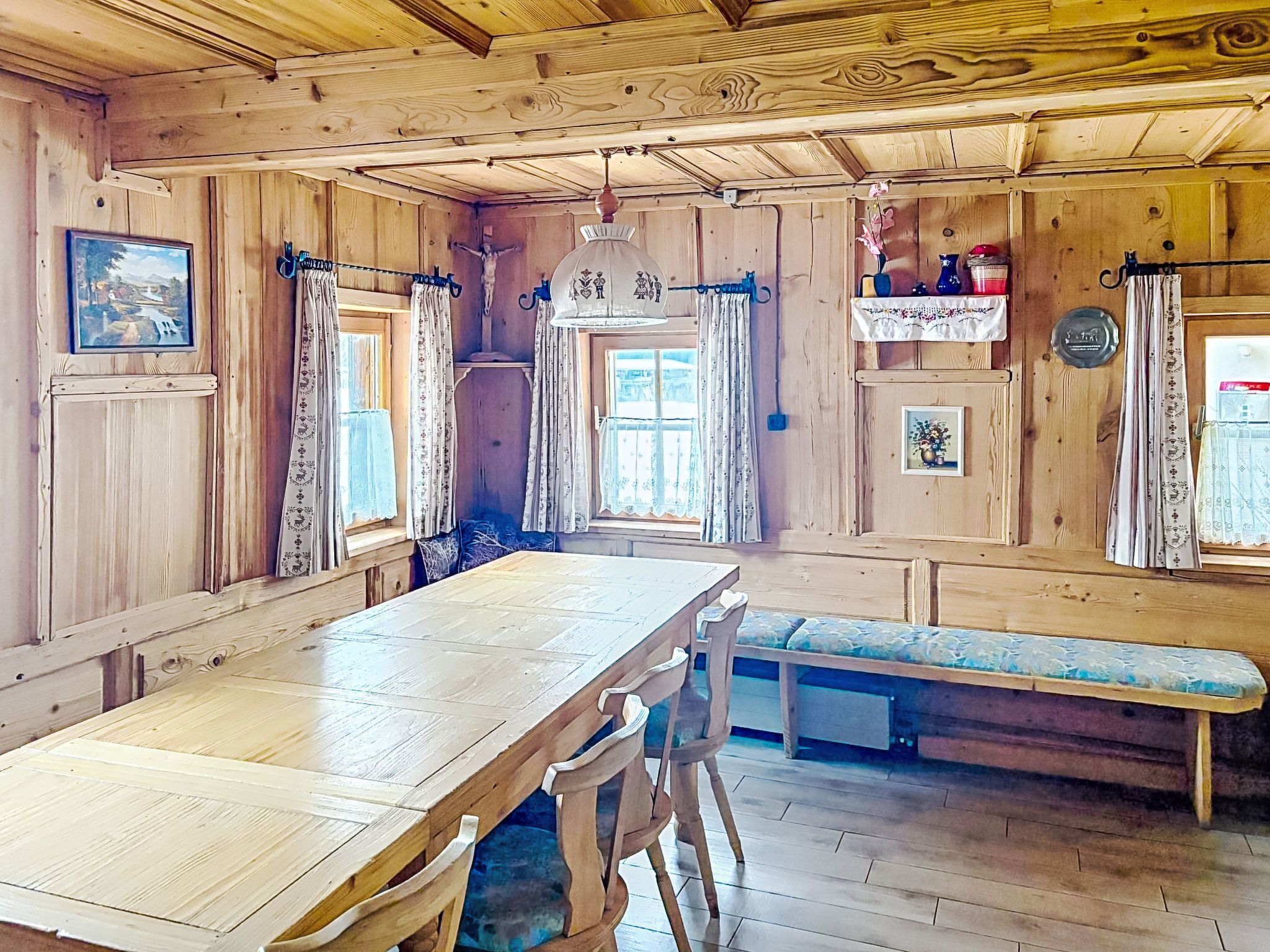 A wooden interior with a long dining table, benches, and a hanging light fixture.