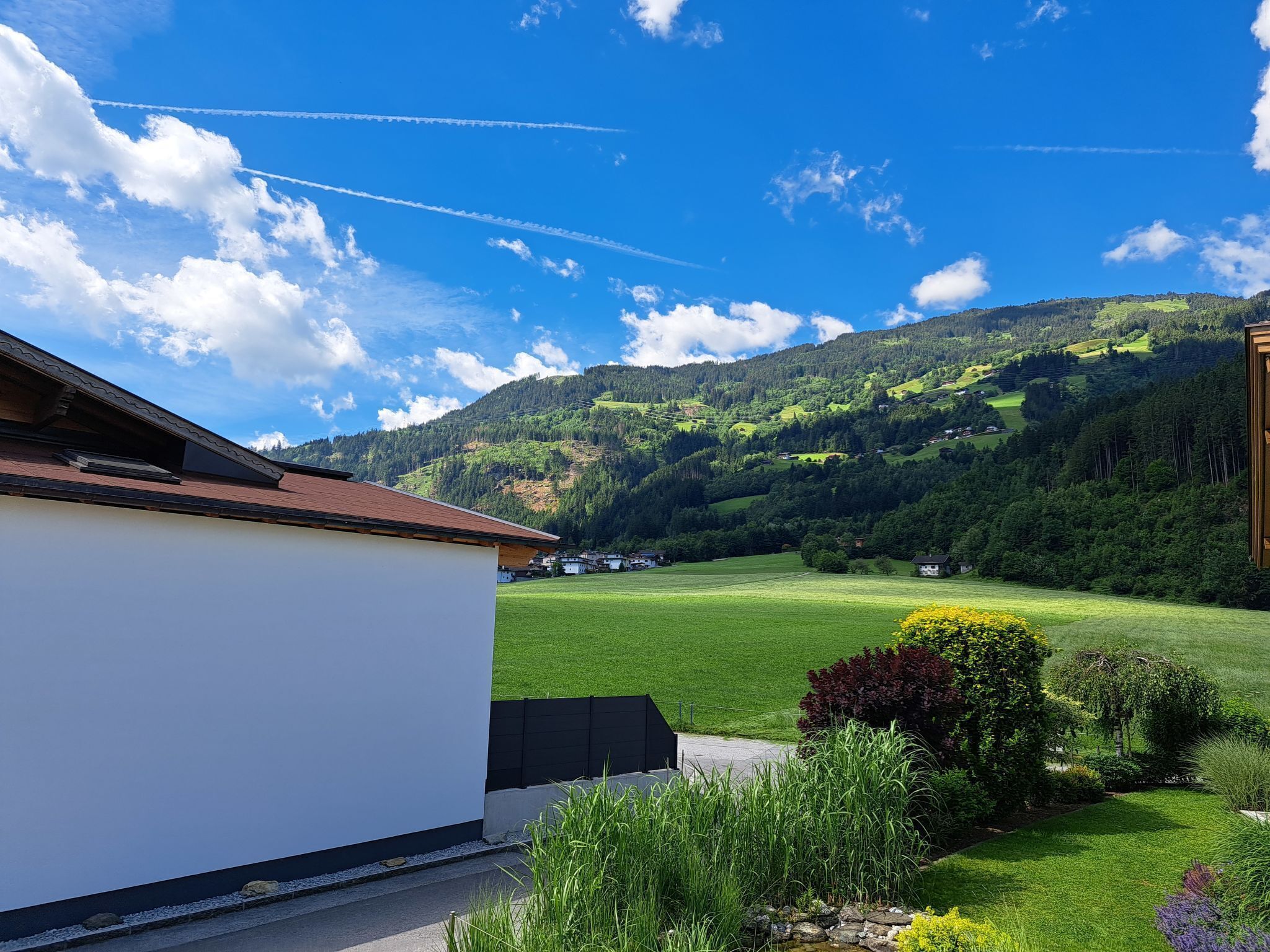 A residential area with a white building, green fields, and a mountain in the background.