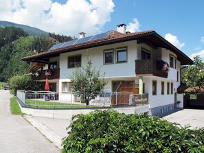 Ein zweistöckiges Haus mit Balkon, Solaranlage und einem kleinen Garten.