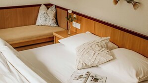 Ein ordentlich bezogenes Bett mit weißen Leinen, ein Nachttisch mit Lampe und eine Wandleuchte.