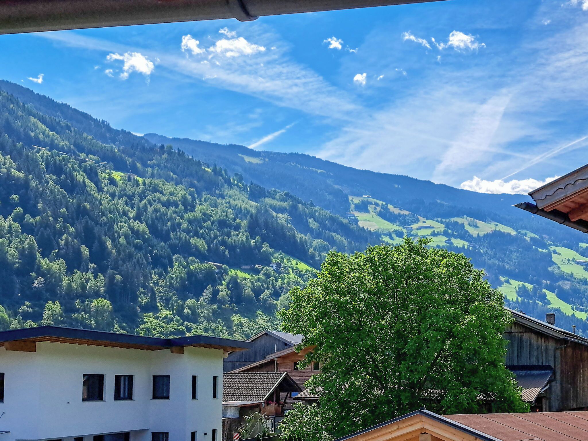 A mountain landscape with a clear sky, a large tree in the foreground, and traditional wooden buildings.