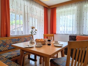 Ein Essbereich mit Holztisch, Stühlen, einer Blumenvase und einem Brotkorb.