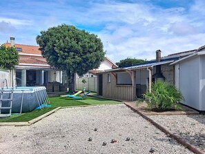 Un jardin avec une piscine, un patio couvert et un espace aménagé avec du gravier où l’on peut jouer à la pétanque.