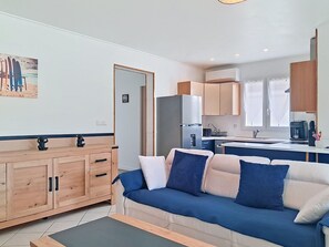 Un salon moderne avec un canapé, un meuble en bois et un coin cuisine équipé de placards et d’un réfrigérateur.