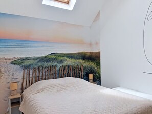 Une chambre avec une fresque murale représentant une plage, un lit, une table de chevet avec une lampe et une fenêtre.
