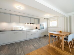 Moderni keittiö, jossa on valkoiset kaapit, puinen ruokapöytä ja ikkuna, jossa on sälekaihtimet.