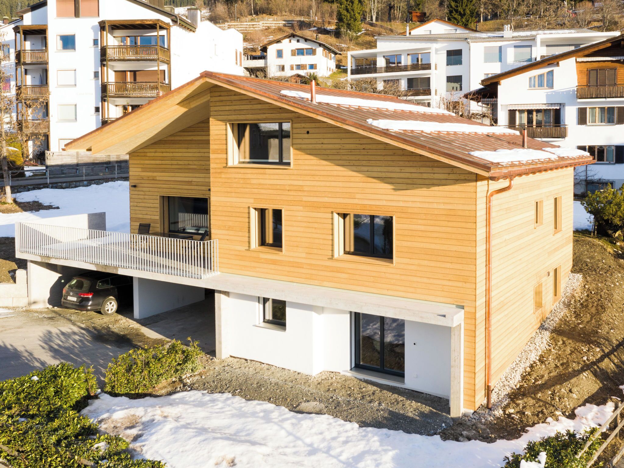 Una casa moderna a due piani con facciata in legno, un balcone e un garage.