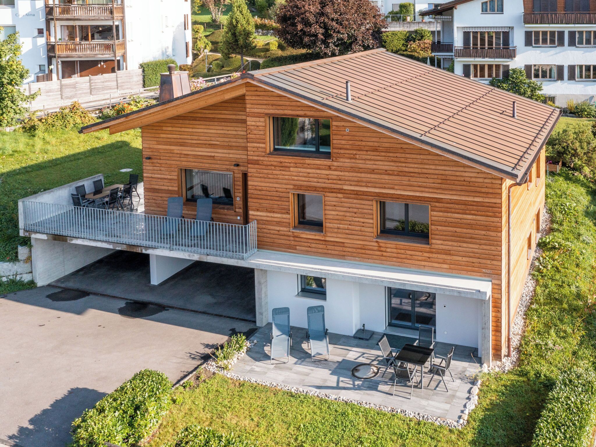 Een modern huis met twee verdiepingen, een houten gevel, een balkon met zitplaatsen en een oprit naar de ingang.