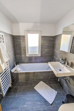A modern bathroom with a bathtub, a sink, and a large mirror. - Armeria by Interhome (Laax)