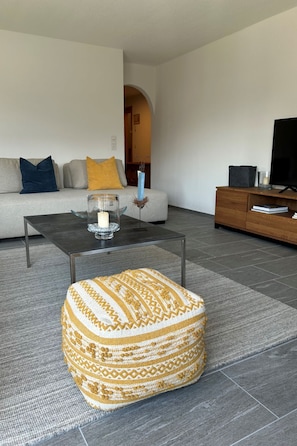 Ein Wohnzimmer mit Sofa, Hocker, Couchtisch und TV-Stand.