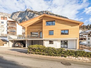 Ein modernes, zweistöckiges Gebäude mit Holzfassade, einem Balkon und Blick auf eine Berglandschaft.