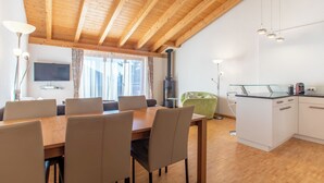 A modern kitchen with wooden beams, a dining area with chairs, a green chair, and a TV.