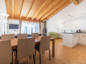 Eine moderne Küche mit Holzbalken, einem Essbereich mit Stühlen, einem grünen Stuhl und einem Fernseher.