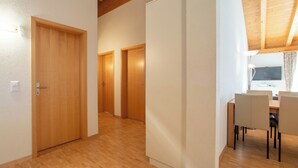 A hallway with wooden flooring, a dining area with chairs and a table, and three wooden doors.