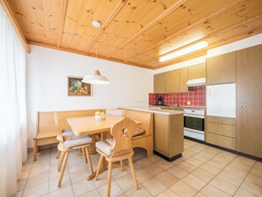 Eine kleine Küche mit Holzschränken, einem Esstisch mit Stühlen, einem Kühlschrank und einer Kaffeemaschine.