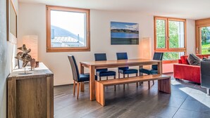 Ein modernes Wohnzimmer mit einem Holzesstisch, blauen Stühlen, einem roten Sofa und großen Fenstern mit Blick ins Freie.