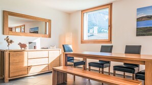 Ein modernes Zimmer mit einem Holztisch, Stühlen, einer Bank, einem großen Spiegel und einem Fenster mit Blick auf die Berge.