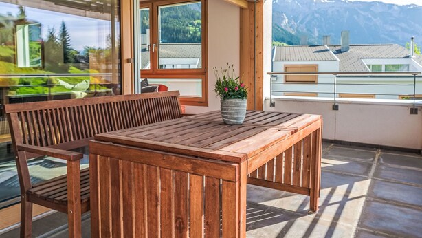Ein Holztisch und eine Bank auf einem Balkon mit Bergblick.