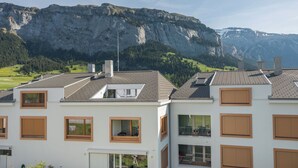 Ein modernes Gebäude mit zahlreichen Fenstern und einer flachen Dachfläche, vor einer Bergkulisse.