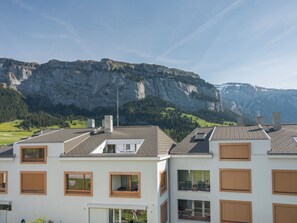 Ein modernes Gebäude mit zahlreichen Fenstern und einer flachen Dachfläche, vor einer Bergkulisse.