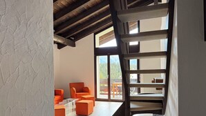 Ein modernes Interieur mit einer Holztreppe, orangefarbenen Sitzgelegenheiten und Blick ins Freie.