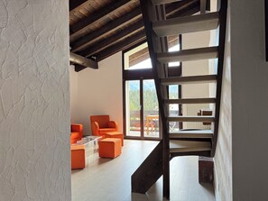 Ein modernes Interieur mit einer Holztreppe, orangefarbenen Sitzgelegenheiten und Blick ins Freie.