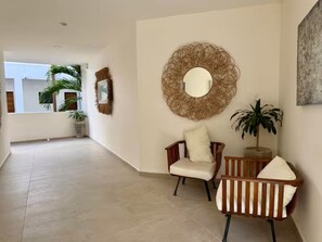 A hallway with a round mirror, two chairs, and a potted plant. - Spacious study with a view of the pool (Q.R.)