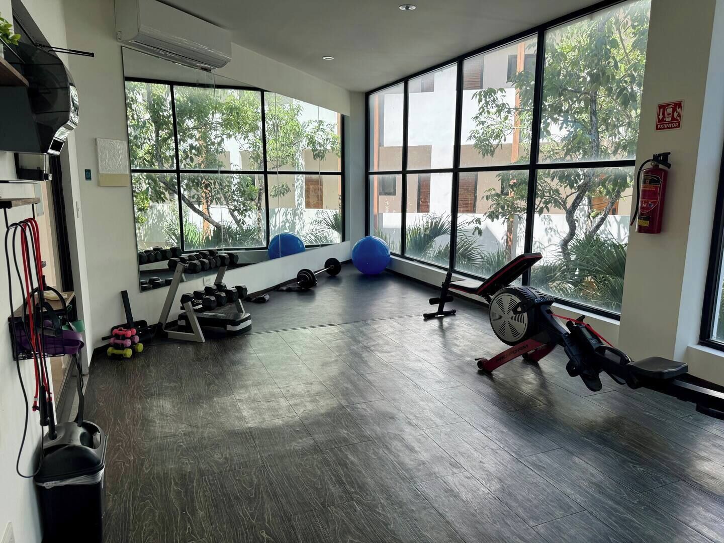 Ein Fitnessraum mit Trainingsgeräten, großen Fenstern und einem Feuerlöscher.