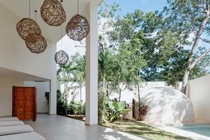 A modern interior with wicker pendant lights, a wooden door, and a pool area with trees and a white wall. - Spacious study with a view of the pool (Q.R.)