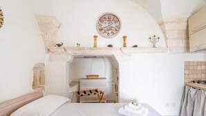 Ein Schlafzimmer mit Bett, einer Holzbank, einem Schminktisch, einer Uhr und einer Küchenzeile.