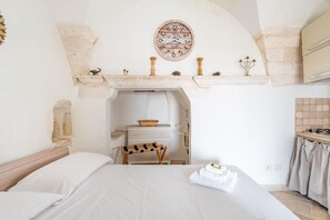 Ein Schlafzimmer mit Bett, einer Holzbank, einem Schminktisch, einer Uhr und einer Küchenzeile.