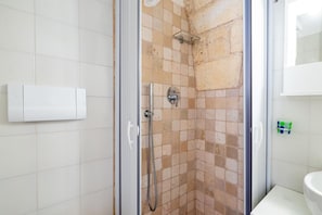 Doccia con porta in vetro, WC bianco e parete rivestita di piastrelle.